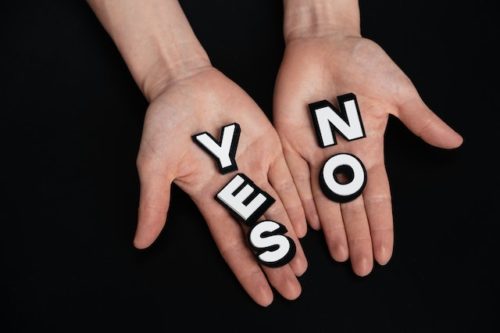Two hands held outright one holding the letters that spell out the word yes, the other holding the letters that spell out the word no.