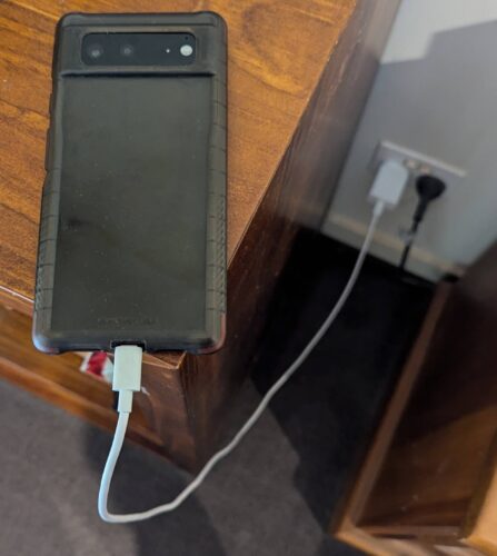 Phone lying face down on table with charging cable plugged in
